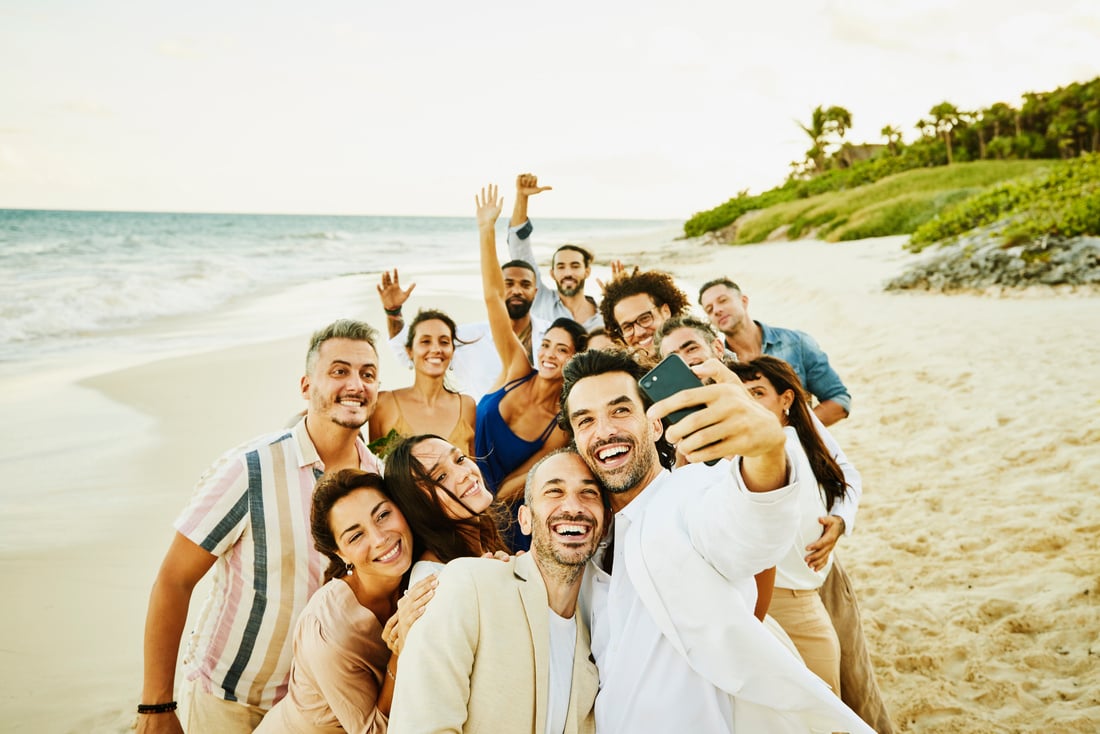 Wide shot of smiling gay couple taking selfie with friends and after wedding ceremony on tropical beach